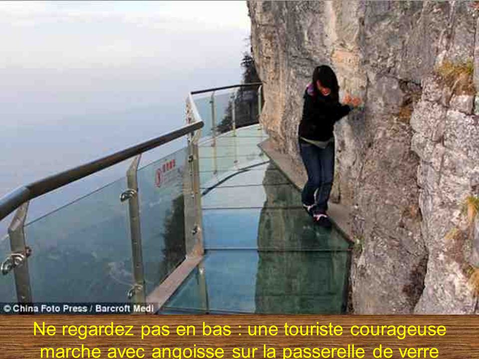 Ne regardez pas en bas : une touriste courageuse marche avec angoisse sur la passerelle de verre